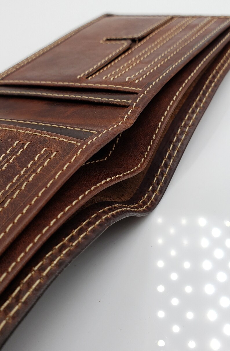 May include: A brown leather wallet with multiple card slots and a billfold. The wallet has a stitched edge with a contrasting light brown thread.
