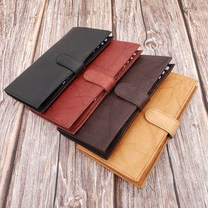 Peut inclure: Quatre journaux reli&eacute;s en cuir noir, rouge, marron et beige. Les journaux sont empil&eacute;s les uns sur les autres, le journal noir en haut. Chaque journal a une fermeture &agrave; boucle.