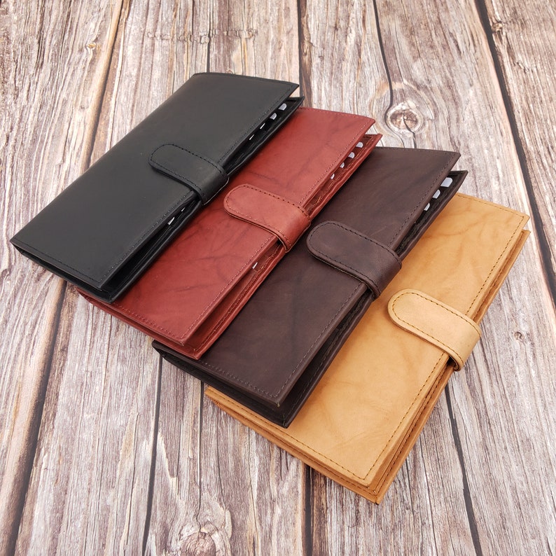 Peut inclure: Quatre journaux reli&eacute;s en cuir noir, rouge, marron et beige. Les journaux sont empil&eacute;s les uns sur les autres, le journal noir en haut. Chaque journal a une fermeture &agrave; boucle.