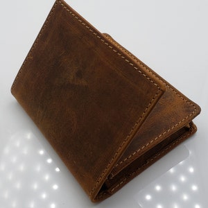 May include: A brown leather wallet with a distressed finish and stitching detail. The wallet is folded in half and the front flap is open.