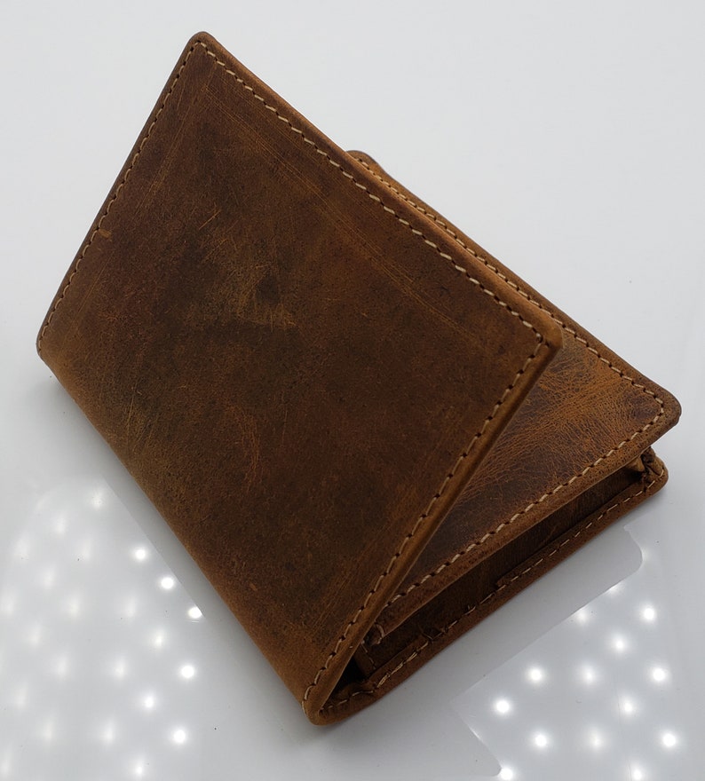 May include: A brown leather wallet with a distressed finish and stitching detail. The wallet is folded in half and the front flap is open.