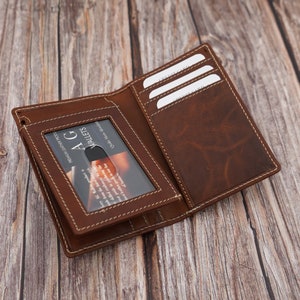 May include: A brown leather wallet with a stitched edge and a clear window for a business card. The wallet has multiple card slots and a fold-over closure.