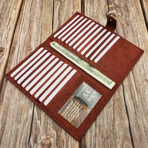 Peut inclure: Un portefeuille en cuir marron avec de multiples fentes pour cartes et une poche pour l'argent liquide. Le portefeuille est ouvert et contient un billet. Le portefeuille a une fen&ecirc;tre transparente qui montre le texte "PREMIUM LEATHER AG WALLETS".