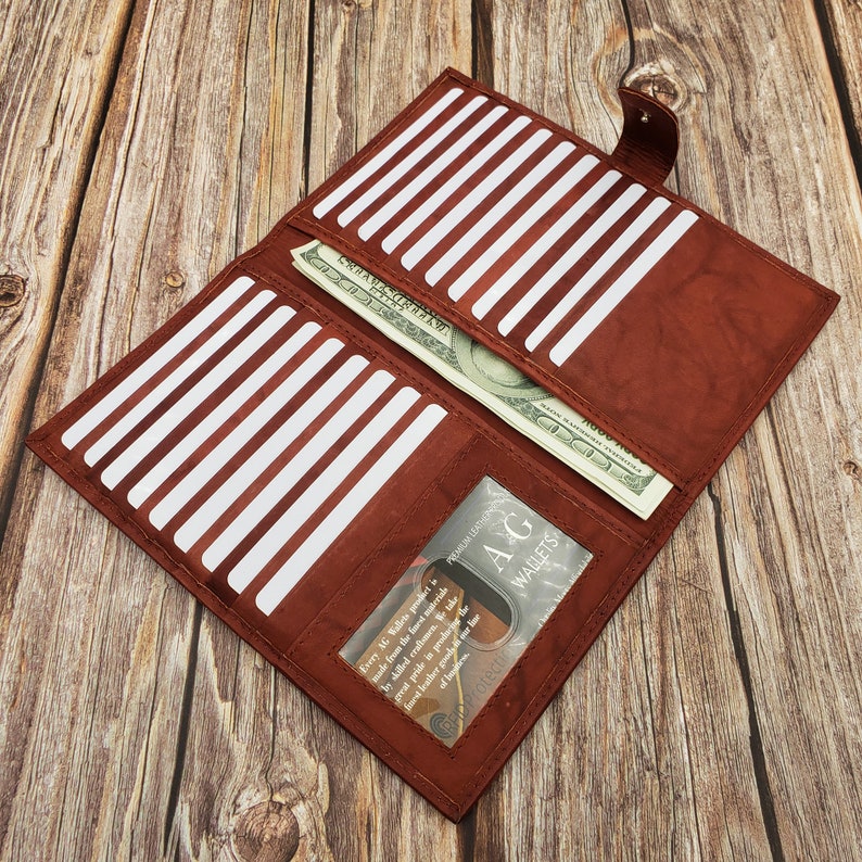 Peut inclure: Un portefeuille en cuir marron avec de multiples fentes pour cartes et une poche pour l'argent liquide. Le portefeuille est ouvert et contient un billet. Le portefeuille a une fen&ecirc;tre transparente qui montre le texte "PREMIUM LEATHER AG WALLETS".