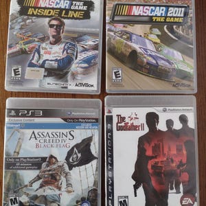 K&ouml;nnte beinhalten: Vier Videospiel-H&uuml;llen f&uuml;r die Playstation 3 Konsole. Die Spiele sind NASCAR The Game Inside Line, NASCAR 2011 The Game, Assassin's Creed IV Black Flag und The Godfather II.