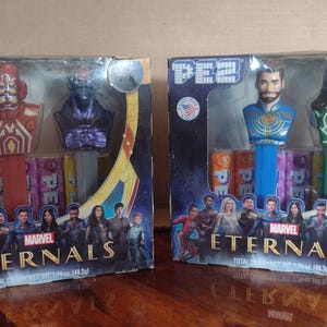 Puede incluir: Dos dispensadores de caramelos PEZ con personajes de la pel&iacute;cula de Marvel Eternals. Una caja tiene dos personajes con detalles en rojo y morado. La otra caja tiene dos personajes con detalles en azul y verde. Cada caja tiene un fondo colorido con el t&iacute;tulo de la pel&iacute;cula.