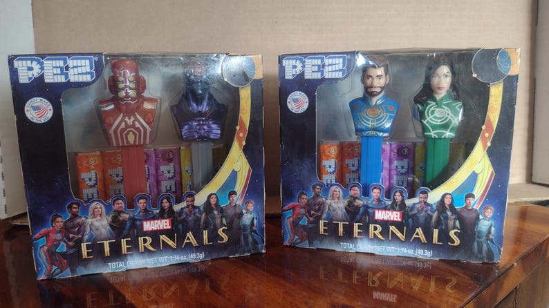 Puede incluir: Dos dispensadores de caramelos PEZ con personajes de la pel&iacute;cula de Marvel Eternals. Una caja tiene dos personajes con detalles en rojo y morado. La otra caja tiene dos personajes con detalles en azul y verde. Cada caja tiene un fondo colorido con el t&iacute;tulo de la pel&iacute;cula.