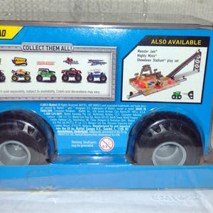 May include: A blue and white cardboard box containing a Monster Jam truck toy. The box features an image of the truck on the front, along with the text "Off-Road" and "Collect Them All!" There's also a picture of a Monster Jam playset with the words "Monster Jam Mighty Minis Showdown Stadium play set".