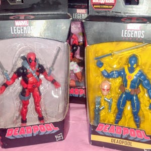 May include: Two Marvel Legends Deadpool action figures in their original packaging. One figure is red and black, the other is blue and yellow. Each figure is holding a sword and comes with additional accessories.