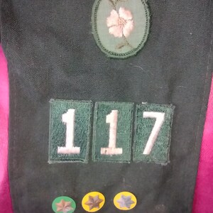 May include: A green fabric patch with the number 117 in white letters. There is a green and pink flower patch above the number patch. There are three small round patches with stars below the number patch.