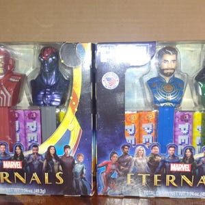 Puede incluir: Dos dispensadores de PEZ con personajes de la pel&iacute;cula Marvel Eternals. Una caja tiene personajes rojos y morados, la otra tiene personajes azules y verdes. Cada caja tiene el logotipo de Marvel Eternals e im&aacute;genes de personajes.
