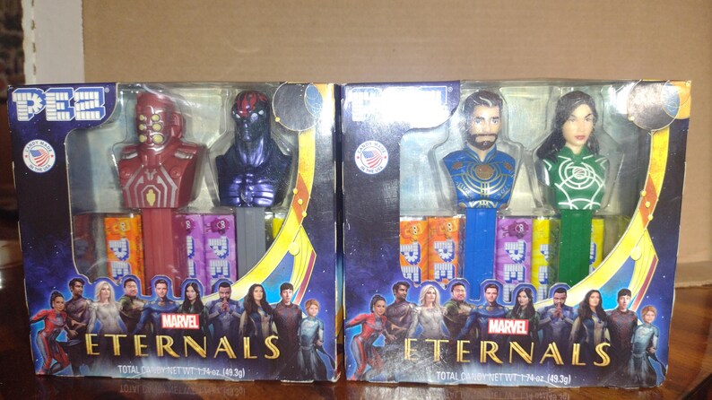 Puede incluir: Dos dispensadores de PEZ con personajes de la pel&iacute;cula Marvel Eternals. Una caja tiene personajes rojos y morados, la otra tiene personajes azules y verdes. Cada caja tiene el logotipo de Marvel Eternals e im&aacute;genes de personajes.