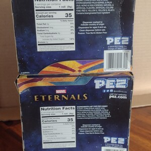 Puede incluir: Dos cajas de caramelos PEZ con el logo de Marvel Eternals. Las cajas muestran informaci&oacute;n nutricional e ingredientes. El logo de PEZ y la direcci&oacute;n del sitio web son visibles. Las cajas est&aacute;n sobre una superficie de madera.