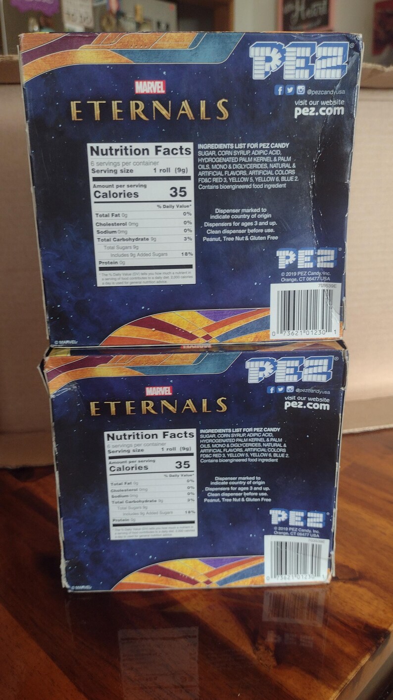 Puede incluir: Dos cajas de caramelos PEZ con el logo de Marvel Eternals. Las cajas muestran informaci&oacute;n nutricional e ingredientes. El logo de PEZ y la direcci&oacute;n del sitio web son visibles. Las cajas est&aacute;n sobre una superficie de madera.