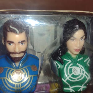Puede incluir: Dos dispensadores de PEZ con bustos de personajes. Uno tiene un uniforme azul con detalles dorados y barba marr&oacute;n. El otro tiene un uniforme verde con detalles blancos y cabello negro. El embalaje es visible.