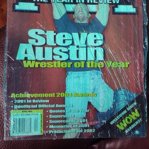 May include: A magazine cover featuring wrestler Steve Austin, titled "PWI The Year in Review." The cover includes text such as "Wrestler of the Year" and "Achievement 2001 Awards." The magazine is encased in plastic.