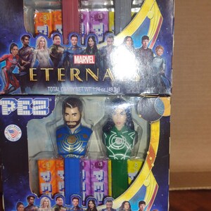 Puede incluir: Dos dispensadores de PEZ con personajes de Eternals de Marvel. El dispensador superior tiene un personaje rojo y dorado y un personaje p&uacute;rpura. El dispensador inferior tiene un personaje azul y dorado y un personaje verde. Cada caja tiene el logo de Marvel Eternals y el texto "PESO NETO TOTAL DE CARAMELOS 49,3 g".