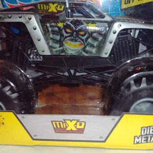 May include: A black and silver Monster Jam die-cast toy truck with a green and black monster face design. The truck is labelled "Max-D" and "Monster Jam".