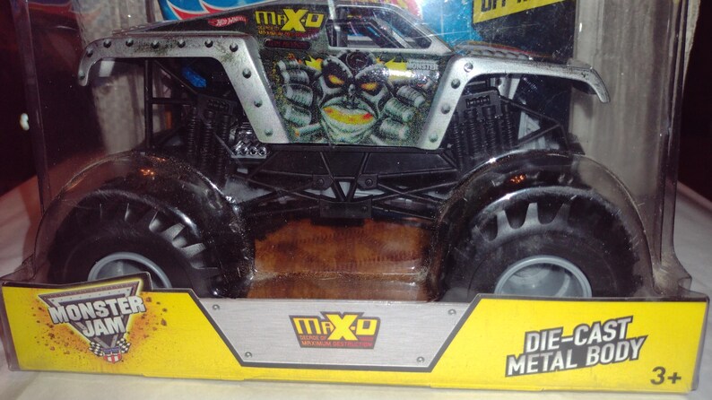 May include: A black and silver Monster Jam die-cast toy truck with a green and black monster face design. The truck is labelled "Max-D" and "Monster Jam".