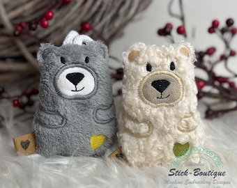 May include: Two plush teddy bears, one gray and one white, with embroidered faces and hearts. The bears are sitting on a white fluffy surface.