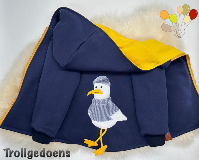 Pu&ograve; includere: Una giacca con cappuccio blu navy con fodera interna giallo brillante e cerniera gialla. Il retro presenta un grafico ricamato di un gabbiano bianco che indossa un maglione lavorato a maglia grigio e un berretto grigio, su zampe palmate.