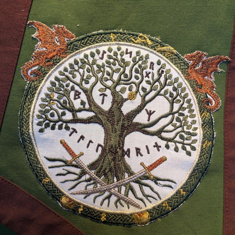 Pu&ograve; includere: Un pannello in tessuto verde con una toppa circolare ricamata. La toppa mostra un albero centrale con foglie verdi, due spade incrociate alla base e due draghi arancioni ai lati. Delle rune sono cucite sullo sfondo di colore bianco.