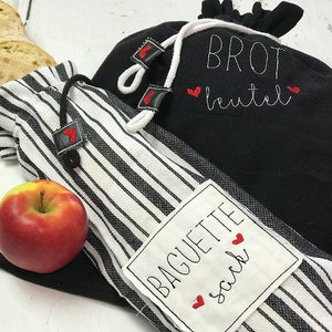 Puede incluir: Dos bolsas de tela negras con rayas blancas y corazones rojos. Una bolsa está etiquetada "BROT beutel" y la otra "BAGUETTE sack".