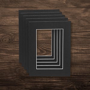 May include: A stack of five rectangular black picture frame mounts, each featuring a crisp white inner bevel edge. The mounts are arranged in a cascading vertical alignment, showcasing the dark matte texture and the clean white border detail.