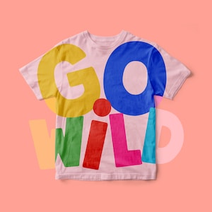 Op de afbeelding: Een lichtroze T-shirt met korte mouwen en de tekst GO WILD in grote, dikke, veelkleurige letters. De G is geel, de O is blauw, de W is groen, de I is rood, de L is roze en de D is lichtblauw, met een rode stip.