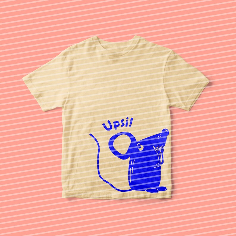 Pu&ograve; includere: Una maglietta beige chiaro con un topo di cartone animato blu e la parola "Upsi!" stampata sul davanti.