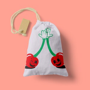 Peut inclure: Un sac en toile blanc avec un motif de cerises rouges et vertes. Les cerises ont des visages souriants et se donnent une tape dans la main.