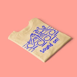 Könnte beinhalten: Ein hellgelbes T-Shirt mit einer blauen Grafik von zwei anthropomorphen Musiknoten mit lächelnden Gesichtern und winkenden Armen. Das Design enthält diagonale weiße Linien und den blauen Schriftzug "Sound on!" in einer verspielten Schrift.