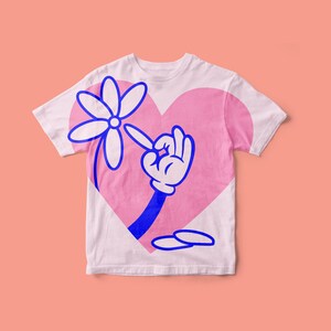 以下が含まれることがあります： ピンクのハートのデザインが施された白いTシャツ。青い手が青い花に手を伸ばしている。花は白い花びらと黄色の芯を持っている。