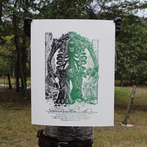 May include: A black and green print of a skeletal figure with tree-like features, holding its arms out. The artwork has a vintage aesthetic and includes text at the bottom. The figure is set against a white background.