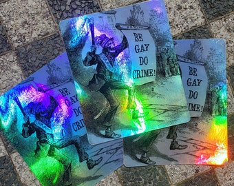 Puede incluir: Cuatro tarjetas holográficas con el texto "BE GAY DO CRIME!" y una ilustración vintage de una figura de esqueleto. Las tarjetas tienen un brillo de arcoíris y están dispuestas sobre una superficie a cuadros.