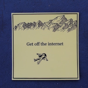 May include: A square, off-white sticker with a black border. The sticker features a mountain range illustration above the text "Get off the internet." Below the text is a small illustration of a person lying down. The background is a dark blue.
