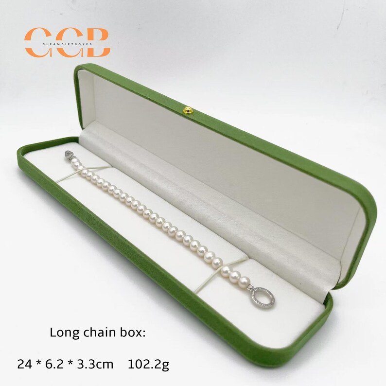 May include: A green jewelry box with a white interior holds a pearl bracelet. The box is rectangular and has a gold clasp. The text "Long chain box: 24 * 6.2 * 3.3cm 102.2g" is printed below the box.