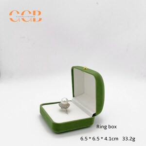 May include: Open green velvet ring box with a white interior. A pearl ring with a silver band sits inside. The box is labeled "Ring box" and measures 6.5 x 6.5 x 4.1 cm and weighs 33.2g.