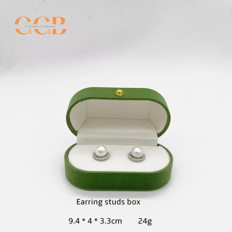 May include: Green velvet earring studs box with a gold clasp, holding two pearl stud earrings. The box measures 9.4 x 4 x 3.3 cm and weighs 24g. The text "Earring studs box" is printed on the box.