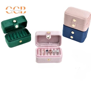 May include: Three velvet ring boxes. One is green, one is pink, and one is a two-tiered box with a pink top and a blue bottom.