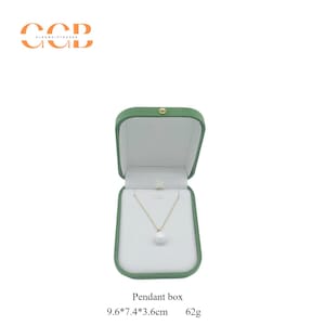 May include: A gold-colored necklace with a white pearl pendant displayed inside a green jewelry box. The box is open, revealing a white interior. The text "Pendant box" is below the box, along with dimensions of 9.6*7.4*3.6 inches and a weight of 62g.
