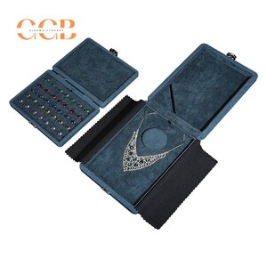 May include: Open blue jewelry display cases with a velvet interior. One case holds a necklace with green gemstones, another holds a collection of colorful gemstones. The cases are open, revealing the jewelry inside.