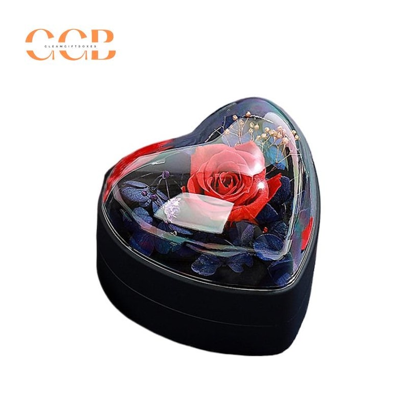 May include: A heart-shaped box with a clear lid, containing a preserved red rose and other dried flowers. The box is black and has a glossy finish.