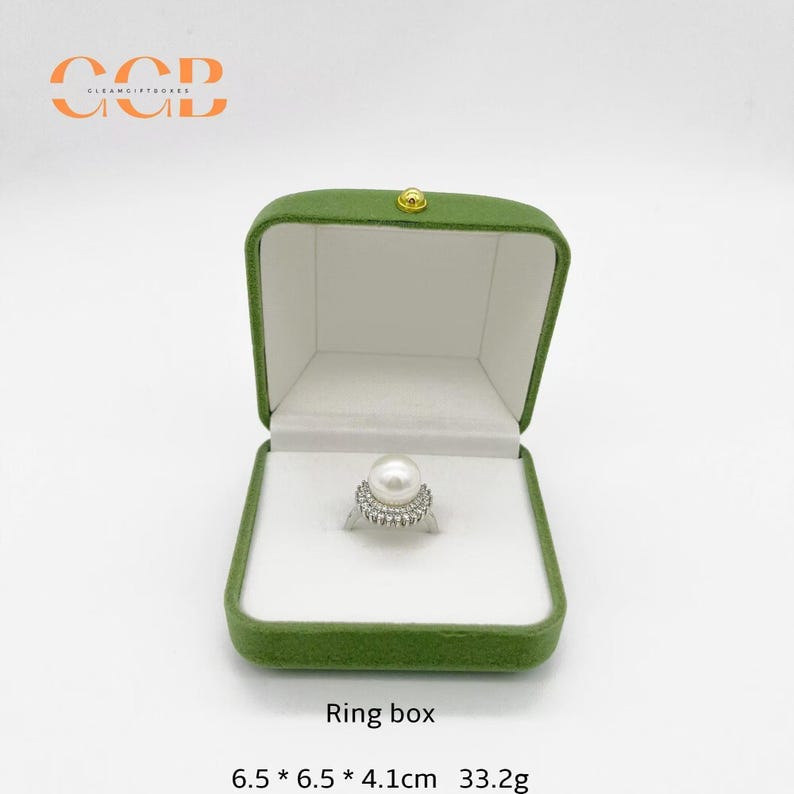 May include: Open green velvet ring box with a white interior, holding a pearl ring. The ring box is labeled "Ring box" and measures 6.5 x 6.5 x 4.1 cm and weighs 33.2g.