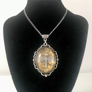 May include: A silver chain necklace with an oval pendant featuring a dragonfly made of gears and clock parts inside a clear resin dome.