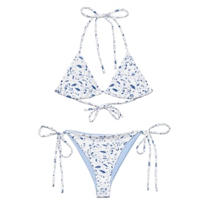 May include: A two-piece bikini set featuring a white base with a blue floral pattern. The top is a halter style with tie closures, and the bottoms are a classic tie-side design. The bikini is designed for swimwear.