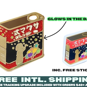 May include: Gold-colored enamel pin of a red and black can with Japanese text that reads "式マクサ スラ、ツロド" and a cartoon of a person blowing bubbles. The pin glows in the dark and includes a free sticker of the same design.