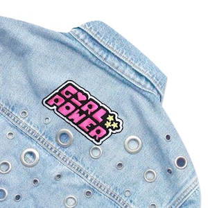 May include: Light blue denim jacket with silver eyelets and a pink and black embroidered patch that says "Girl Power" with a heart and stars.