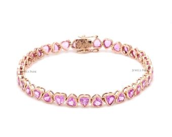 May include: A delicate pink sapphire heart-shaped tennis bracelet with a rose gold setting. The bracelet is made of small, heart-shaped sapphires that are set close together. The bracelet is secured with a clasp.