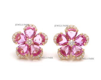 May include: A pair of gold flower-shaped earrings with pink sapphires and diamonds. The earrings are set in a delicate floral design with a central diamond surrounded by pink sapphires.